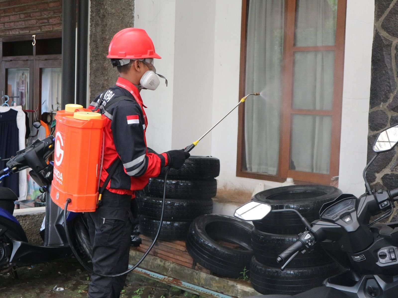 Technicien en équipement de protection pulvérisant un traitement le long d'un bâtiment, barrière posée avant intervention intérieure